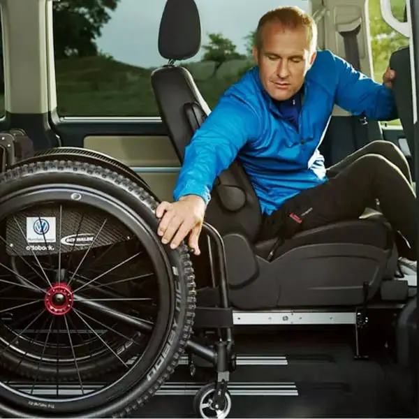Mann sitzt in einem behindertengerechten Auto und greift nach seinem Rollstuhl